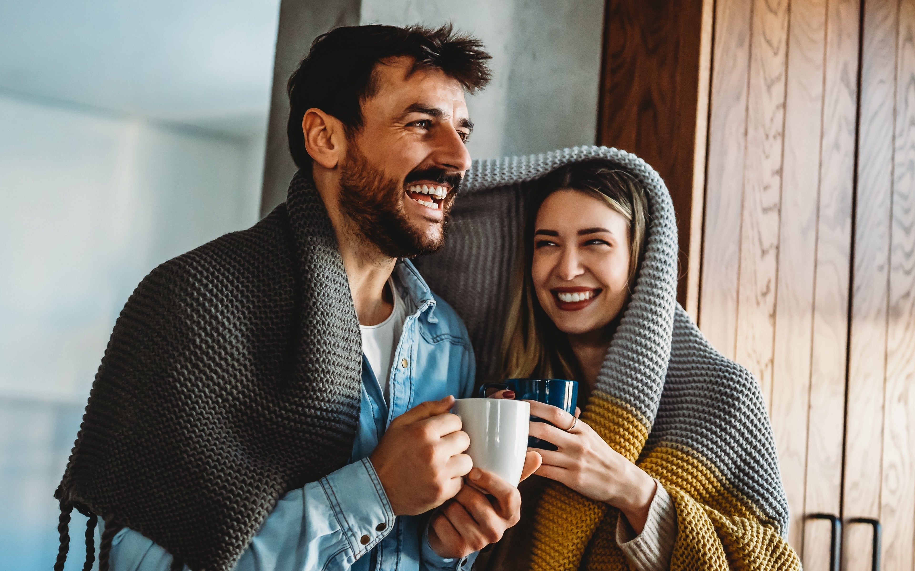 man and woman wrapped in blanket drinking from mugs